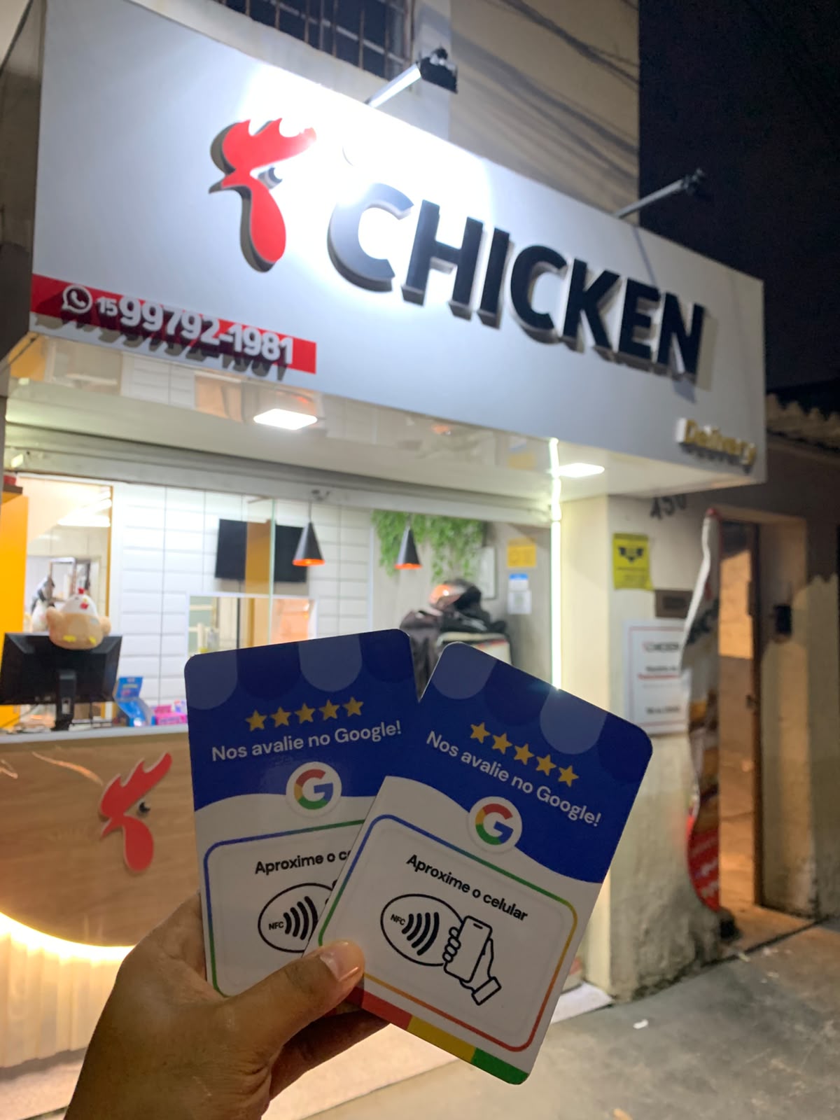Mão segurando duas placas de avaliação em frente a uma lanchonete iluminada à noite