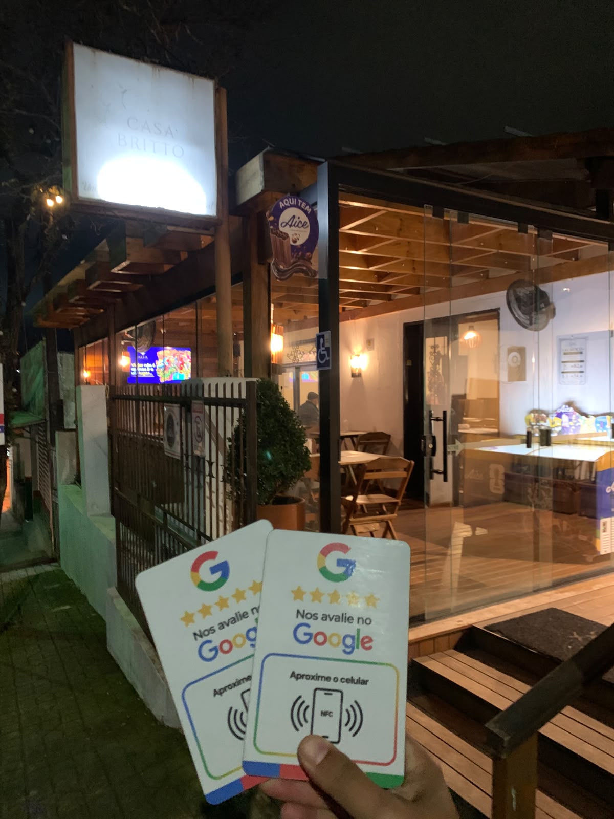Mão segurando duas placas de avaliação em frente ao restaurante Casa Britto à noite